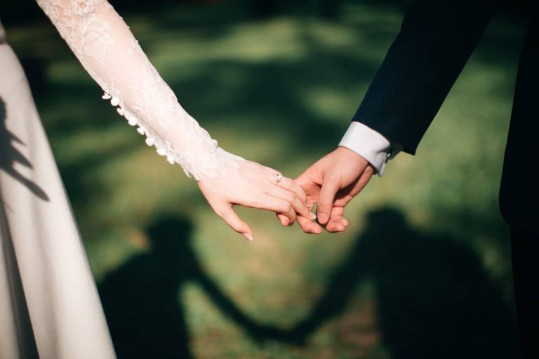 Novios cogidos de la mano con sus sombras en el césped