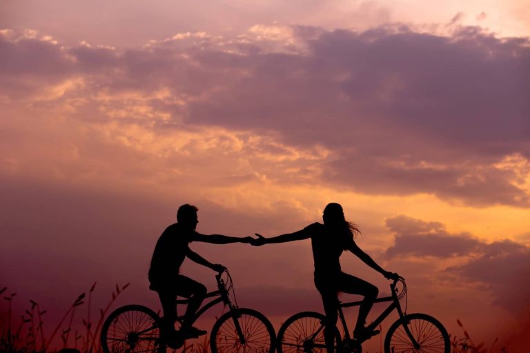 Pareja en bicicleta dándose la mano al atardecer