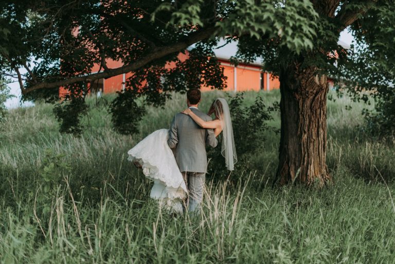 Novios abrazados de espaldas junto a un árbol en el campo
