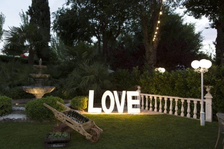 Letras luminosas «LOVE» en un jardín con fuente al anochecer