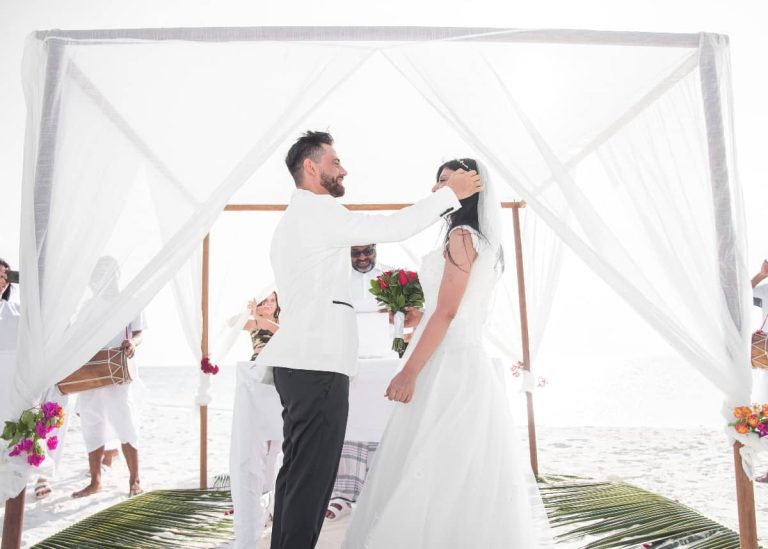 Novios bajo un dosel blanco en una ceremonia en la playa