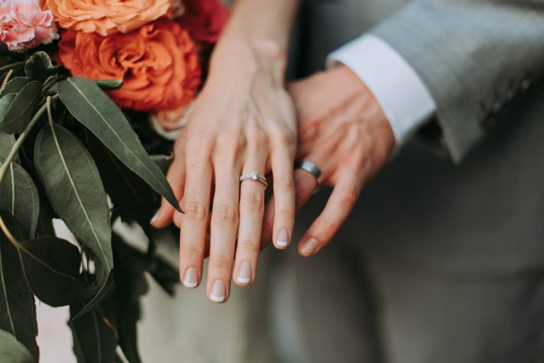 Manos de los novios con las alianzas junto al ramo
