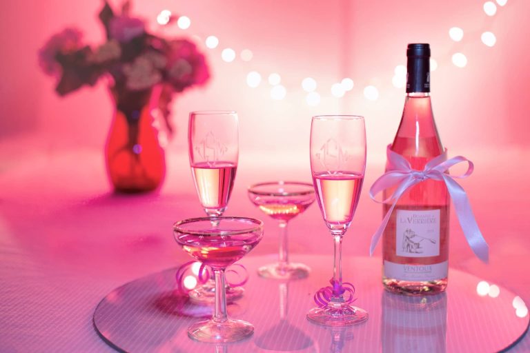 Copas y botella de vino rosado sobre una mesa con luces rosas