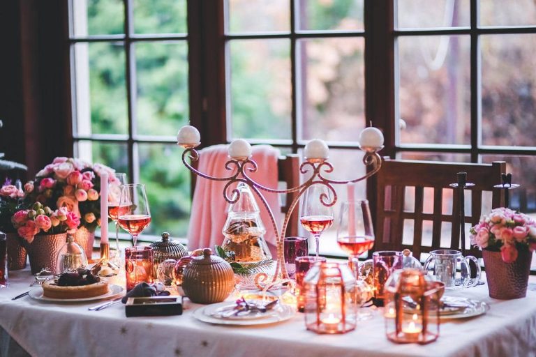 Mesa decorada con flores, copas y farolillos junto a un ventanal